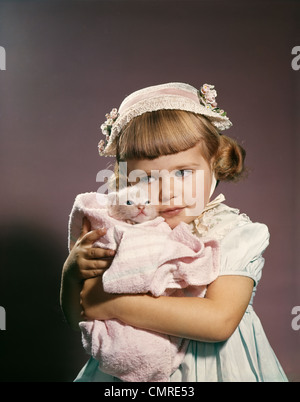 1950S 1960S KLEINES MÄDCHEN IN OSTERN HUT UMARMT EINE KÄTZCHEN Stockfoto