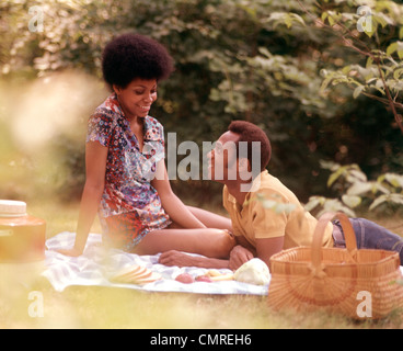 1970ER JAHREN ROMANTISCHE AFROAMERIKANISCHEN PAAR MANN FRAU PICKNICKKORB SITZT GRASS Stockfoto