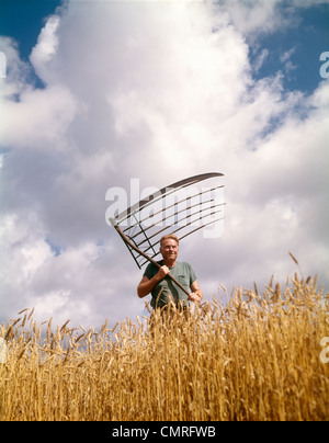 1970ER JAHRE BAUER MANN IN WEIZEN FELD HOLDING ANTIKE KORN WIEGE Stockfoto