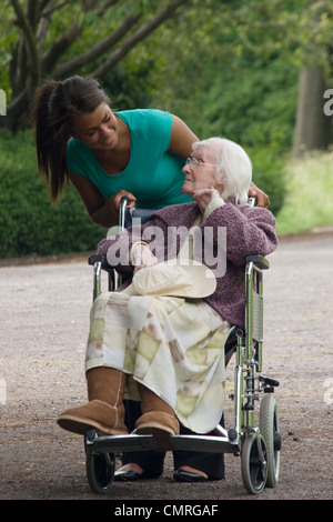 junge Frau drängen ältere Dame im Rollstuhl in den park Stockfoto