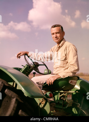 1960ER JAHRE PORTRAIT LÄCHELND MANN BAUER SITZT AUF GRÜNEN TRAKTOR RAUCHEN ZIGARETTE Stockfoto