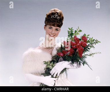 1960ER JAHREN FRAU PROM QUEEN TRAGEN WEIßE ABENDKLEID HOLDING BOUQUET BLUMEN ROTE ROSEN BLICK IN DIE KAMERA Stockfoto