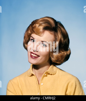 1960ER JAHREN LÄCHELND BLONDE FRAU TRÄGT EINEN GELBEN PULLOVER GENEIGTEM KOPF FRAGENDEN AUSDRUCK Stockfoto