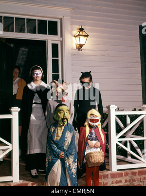 1960ER JAHRE GRUPPE KINDER IN HALLOWEEN-KOSTÜMEN AUF VERANDA SÜßES ODER SAURES Stockfoto