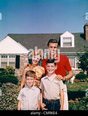 PORTRÄT LÄCHELND FAMILIE VATER MUTTER ZWEI SÖHNE ZUSAMMEN STEHEN VOR VORSTADTHAUS OUTDOOR-1960ER JAHRE Stockfoto