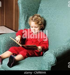 1970ER JAHREN KLEINKIND MÄDCHEN SITZEN IM STUHL LESUNG BUCH RETRO Stockfoto