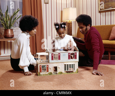 1970ER JAHRE AFRO-AMERIKANISCHE FAMILIE MUTTER VATER TOCHTER PLAING MÄDCHEN STOCK MIT DOLLHOUSE DOLL HOUSE RETRO Stockfoto