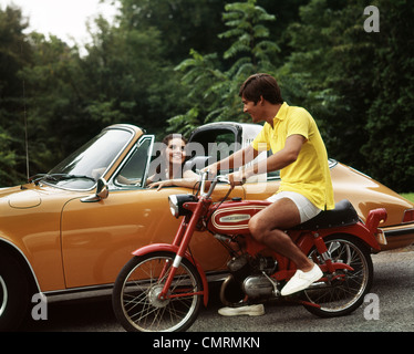 1970ER JAHREN LIFESTYLE SPRECHEN FLIRT PAAR MANN AUF KLEINE ROTE HARLEY DAVIDSON MOTORRAD LÄCHELNDE FRAU IN ORANGE PORSCHE AUTOMOBIL Stockfoto