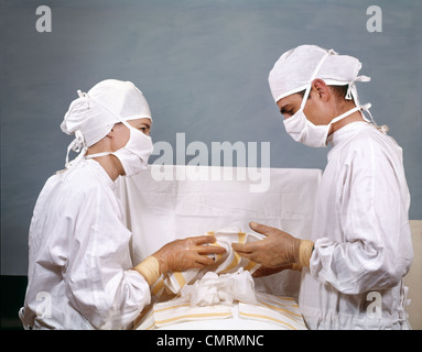 1950S 1960S ARZT & KRANKENSCHWESTER IN CHIRURGIE BETRIEB BETRIEB STERILE CHIRURGISCHE WEIßE MÜTZEN KLEIDER MASKEN RETRO VINTAGE Stockfoto