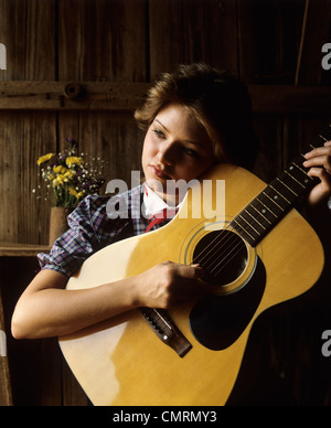 1980ER JAHREN NACHDENKLICHE JUNGE FRAU SPIELEN SECHS ZEICHENKETTE AKUSTIKGITARRE Stockfoto