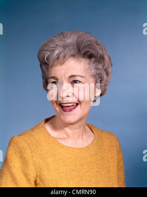 1960ER JAHRE PORTRAIT LÄCHELND SENIORIN TRAGEN ORANGE TOP Stockfoto