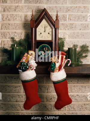 1970ER JAHREN WEIHNACHTEN STILLLEBEN ANTIKEN KAMIN MANTEL CLOCK STRÜMPFE VOLLER GESCHENKE CANDY CANES Stockfoto