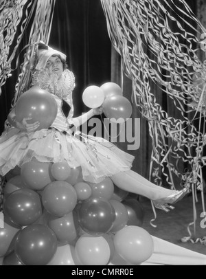 1920ER JAHREN FRAU GEKLEIDET IN HARLEKIN KOSTÜM SITZEN AUF STAPEL VON LUFTBALLONS Stockfoto