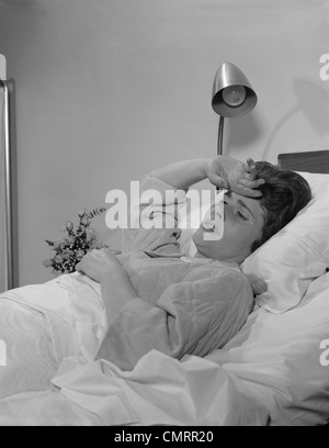 1960ER JAHRE FRAU-KRANKEN IM KRANKENHAUS-BETT HAND LIEGEND ZUR STIRN GEDRÜCKT Stockfoto