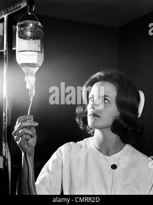 1960ER JAHREN FRAU KRANKENSCHWESTER IN GAP UND EINHEITLICHE IN ANPASSUNG VON IV-FLASCHE FLIEßEN Stockfoto