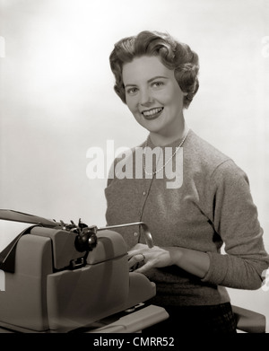 1950ER JAHREN LÄCHELND PORTRAIT SEKRETÄR HINTER SCHREIBMASCHINE SITZEN Stockfoto