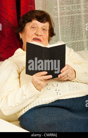 Ältere Frau sitzen auf der Couch und Lesebuch in ihrem Haus Stockfoto