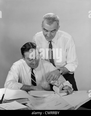 1960ER JAHREN 2 GESCHÄFTSLEUTE IN HEMDSÄRMELN MIT BLICK AUF PAPIERKRAM Stockfoto