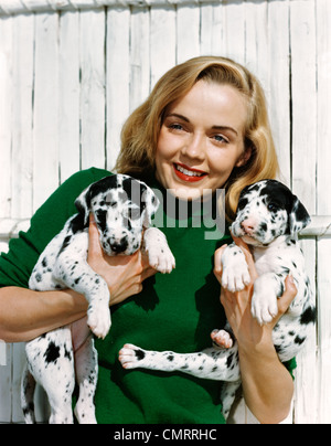 1950ER JAHRE PORTRAIT LÄCHELND TEEN MÄDCHEN TRAGEN GRÜNE PULLOVER HÄLT ZWEI DALMATINER WELPEN Stockfoto