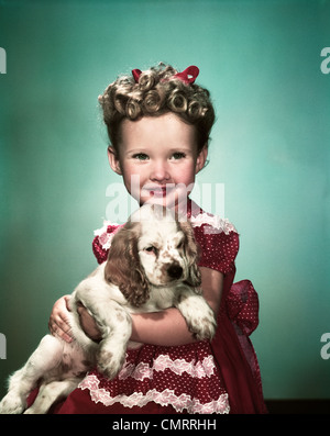 1940ER JAHRE PORTRAIT LÄCHELND MÄDCHEN TRAGEN ROT GEPUNKTETEN KLEID HÄLT COCKER SPANIEL WELPEN Stockfoto