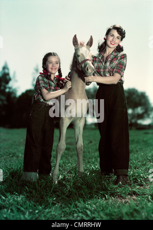 1940S 1950S LÄCHELNDE MÄDCHEN UND TEENAGER-MÄDCHEN TRAGEN PASSENDE KARIERTE HEMDEN UND JEANS POSIERT MIT PONY COLT Stockfoto