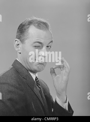 1950S 1960S MANN ZWINKERT AUGE MACHT ORDNUNG GESTE MIT DAUMEN UND ZEIGEFINGER BLICK IN DIE KAMERA Stockfoto