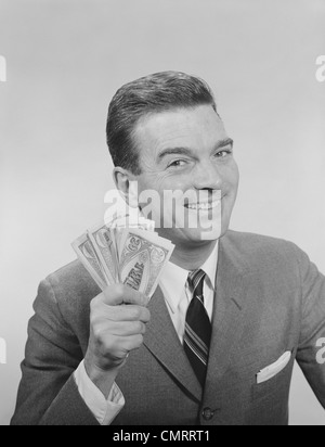 1950S 1960S LÄCHELNDER MANN HÄLT EINE HANDVOLL GELD GEFÄLSCHTE RECHNUNGEN BLICK IN DIE KAMERA Stockfoto