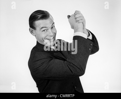 1950S 1960S LÄCHELND GESCHÄFTSMANN HÄNDE VERSCHRÄNKT OVERHEAD IN ERFOLGREICHEN SIEGER SYMBOLISCHES ZEICHEN Stockfoto