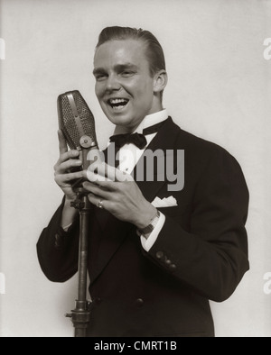 1920S 1930S LÄCHELN MANN RADIO SÄNGER ENTERTAINER CROONER IM SMOKING INS MIKROFON SINGEN Stockfoto