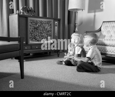 1960ER JAHRE STOCK BRUDER & SCHWESTER SITTING ON WOHNZIMMER VOR DEM FERNSEHER Stockfoto