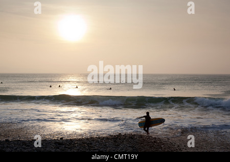 Eine Surfer verlässt das Wasser bei Godrevy, St Ives Bay, Cornwall, während die Sonne untergeht. Stockfoto