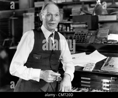 1930S 1940S ÄLTERER MANN MIT SHIRTSLEEVES WESTE STÜTZTE SICH AUF TYP SCHUBLADENSCHRANK IN ALTEN DRUCKEN SHOP RAUCHEN ZIGARRE UND SPRECHEN Stockfoto