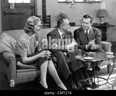 1930S 1940S COUCH, ZWEI MÄNNER UND FRAU SOZIALE GRUPPE SITZEN WEITER SPRECHEN INDOOR Stockfoto