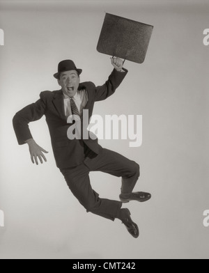 1950S 1960S AUFGEREGT, GLÜCKLICH GESCHÄFTSMANN MIT AKTENKOFFER SPRINGEN LUFT KLICK FERSEN ZUSAMMEN MIT BLICK AUF KAMERA SCHREIEN Stockfoto