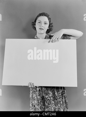 1930S 1940S FRAU MIT LEEREN PLAKAT SCHILD HAND VON OBEN BLICK IN DIE KAMERA, BLICK IN DIE KAMERA ZEIGEN Stockfoto