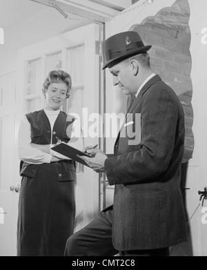 1960ER JAHRE MANN MIT ZWISCHENABLAGE IM GESPRÄCH MIT FRAU IN TÜR Stockfoto