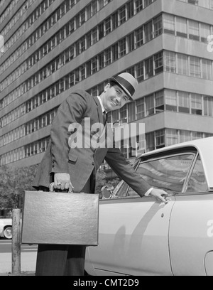 1960ER JAHRE GESCHÄFTSMANN MIT AKTENKOFFER INS AUTO AUF URBAN STREET Stockfoto