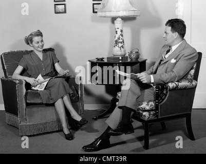 1940ER JAHREN PAAR SITZT IM WOHNZIMMER LESEN MANN FRAU MITEINANDER ZU REDEN Stockfoto