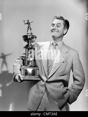 1950S 1960S STOLZER MANN LÄCHELND, EINE FUßBALL-TROPHÄE BLICK IN DIE KAMERA HALTEN Stockfoto