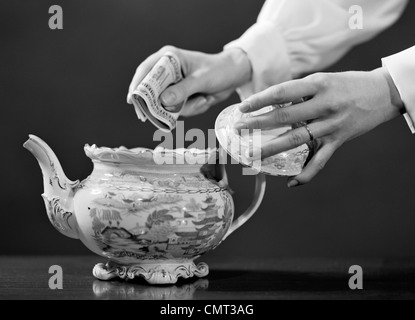 1950ER JAHREN FRAU HÄNDE SETZEN BÜNDEL GELDSCHEINE IN TEEKANNE Stockfoto