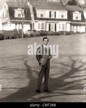 1950ER JAHRE MANN GEHOBENEN GESCHÄFTSMANN EXECUTIVE IN GRAUEN FLANELL-ANZUG UND KRAWATTE AUF S HAUS RASEN STEHEN Stockfoto