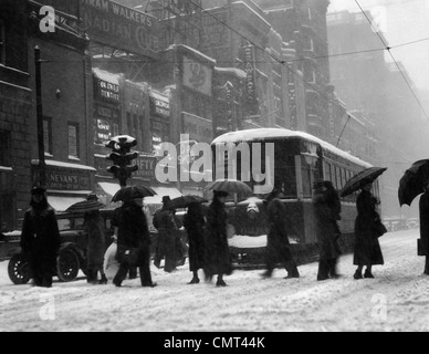 1920S 1930S MASSE MIT SONNENSCHIRMEN KREUZUNG STRAßE VOR STRAßE AUTO TROLLEY WÄHREND SCHNEESTURM Stockfoto