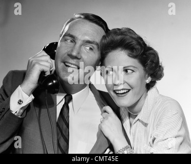 1950S 1960S MANN AM TELEFON FRAU LEHNT IN INDOOR HÖREN SPRECHEN Stockfoto