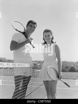 1960ER JAHRE PORTRAIT TENNIS PAAR MANN FRAU SCHLÄGER NETZ STAND HALTEN Stockfoto