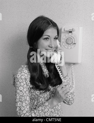 1960S 1970S LÄCHELN AUF DEN LIPPEN TEENAGER-MÄDCHEN AM ROTARY WAND TELEFON SPRECHEN Stockfoto