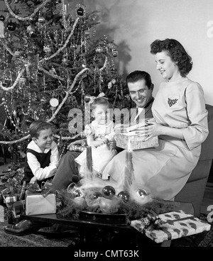 1940ER JAHRE FAMILIE VATER SOHN TOCHTER SITZEN ZUSAMMEN VOR WEIHNACHTEN BAUM MUTTER ERÖFFNUNG GEGENWART Stockfoto