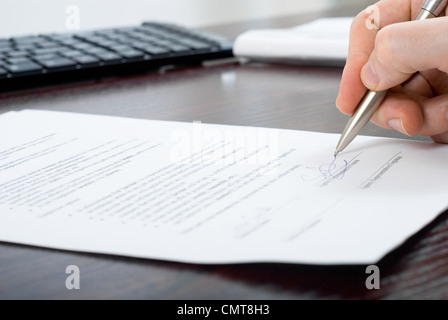 Hautnah-Shooting der Unterzeichnung Vertrag durch einen Unternehmer mit Silberstift an seinem Arbeitsplatz Stockfoto