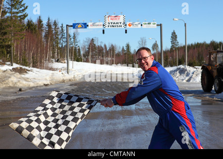 Ein Mann im Motorsport Overall winkt eine Zielflagge vor einer Start- und Ziellinie. Stockfoto