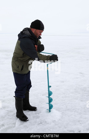 Ein Mann geht Eisfischen bohrt ein Loch in der Oberfläche der See Näsijärvi in Tampere, Finnland. Stockfoto