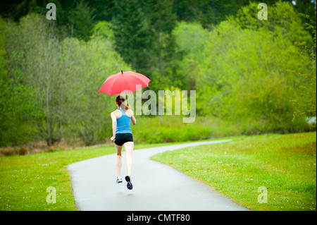 Gemischte Rassen Läufer training auf remote-Straße mit Regenschirm Stockfoto